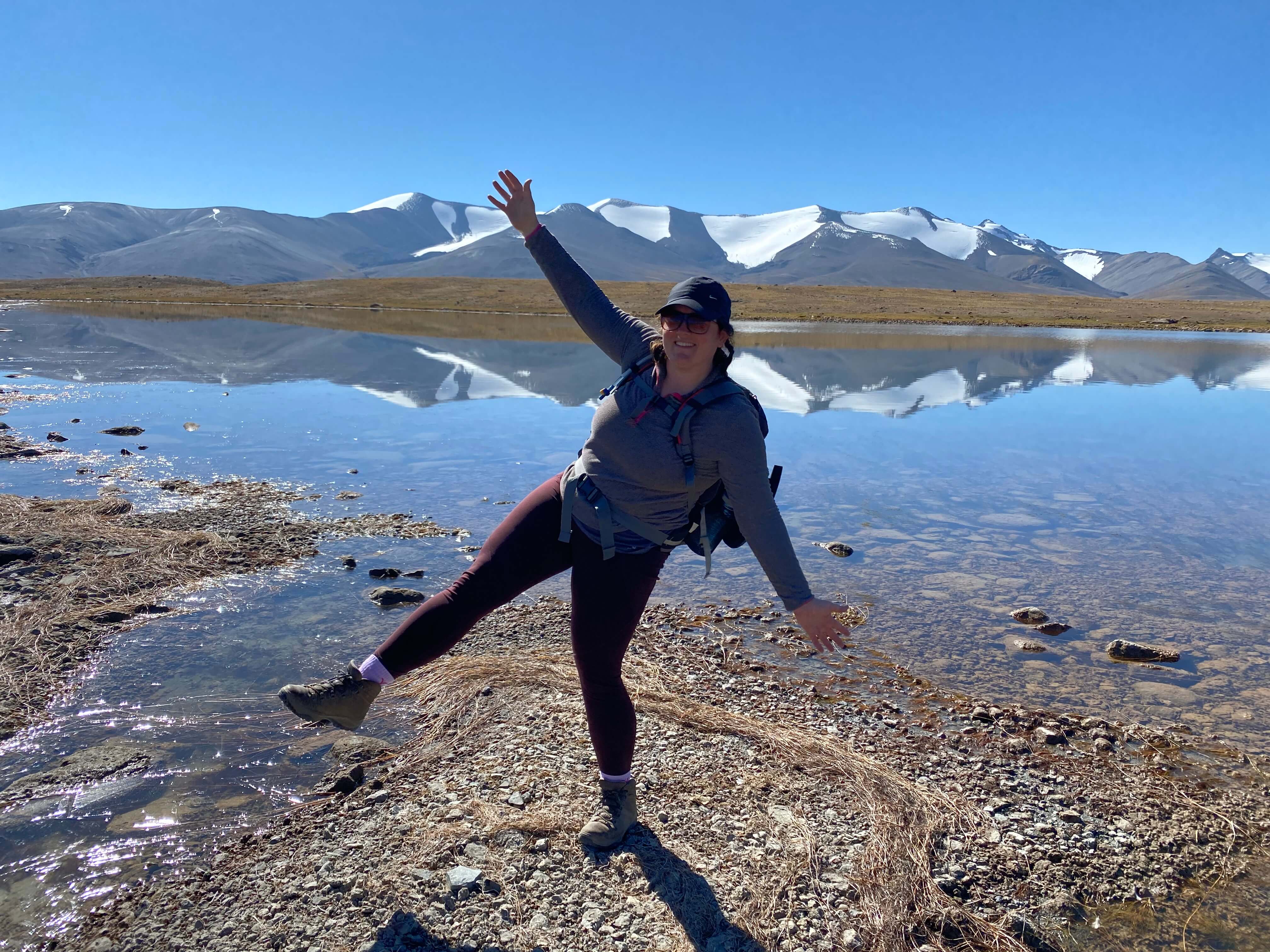 lydia posing in front of small lake with snowcapped mountains behind