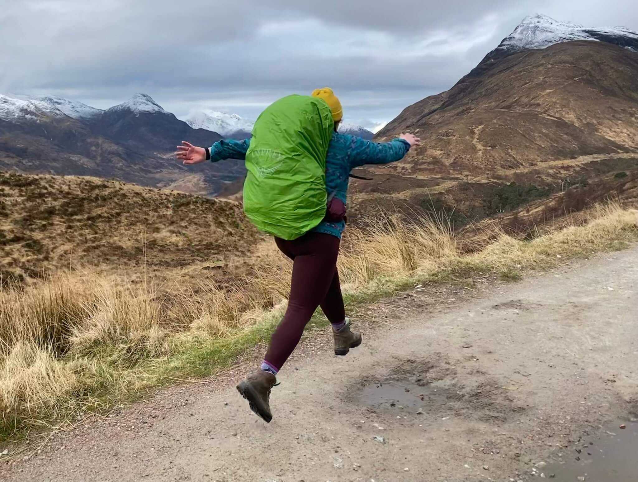 lydia leaping with backpack on with mountains behind